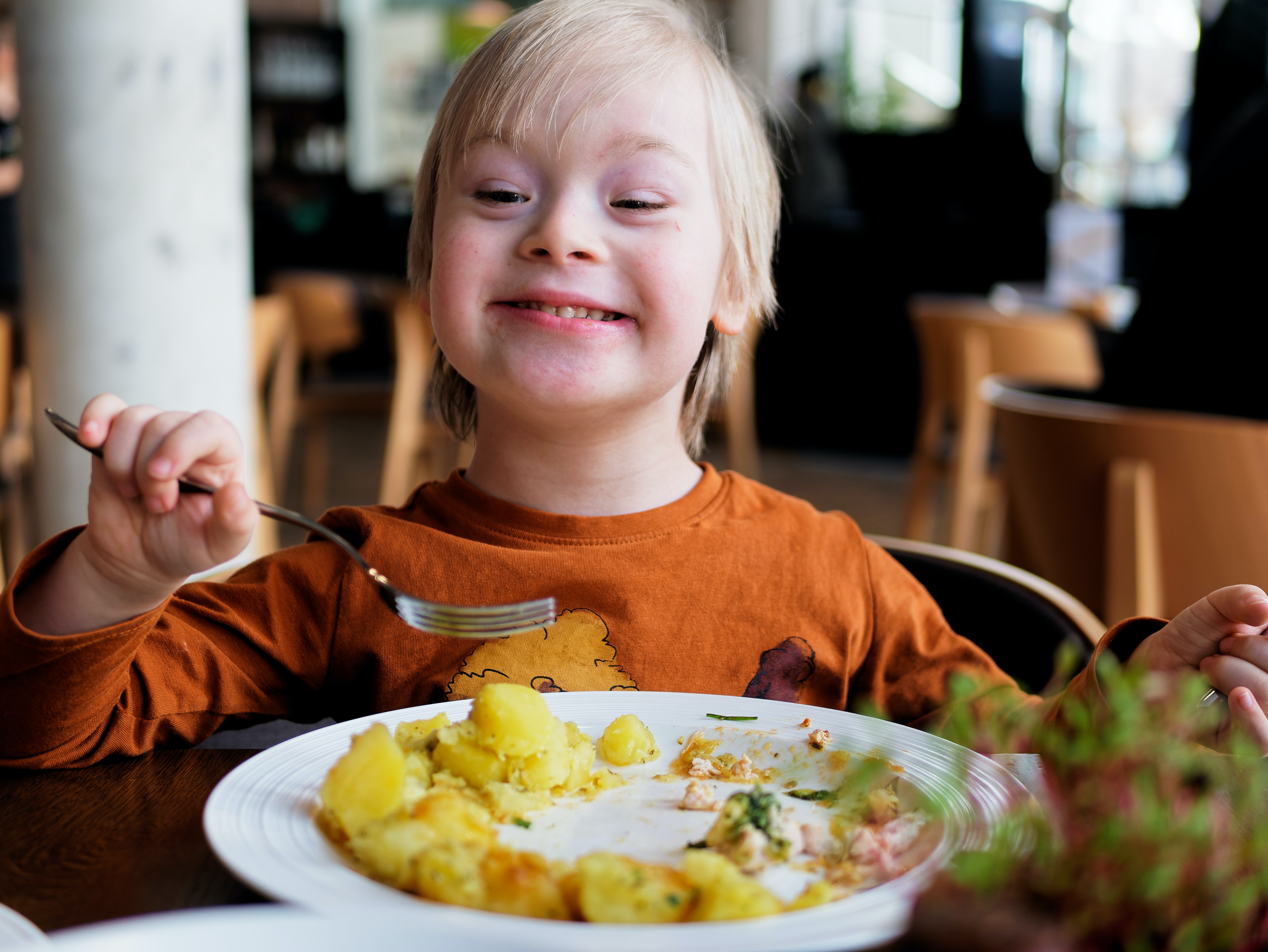 Child with Down Syndrome eating breakfast and smiling